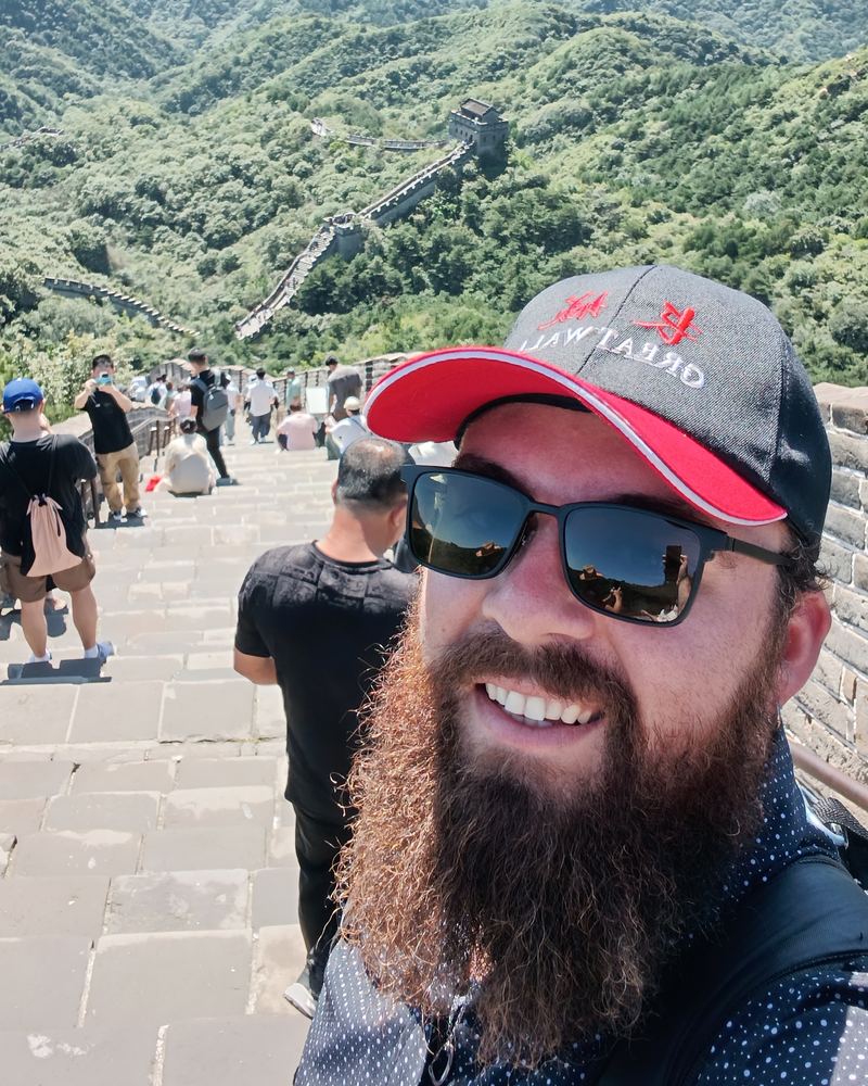 Teacher Reed smiling on the Great Wall with green mountains behind