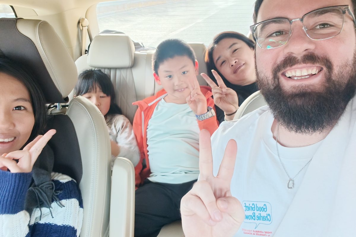 Teacher Reed in a car selfie with a smiling family making peace signs