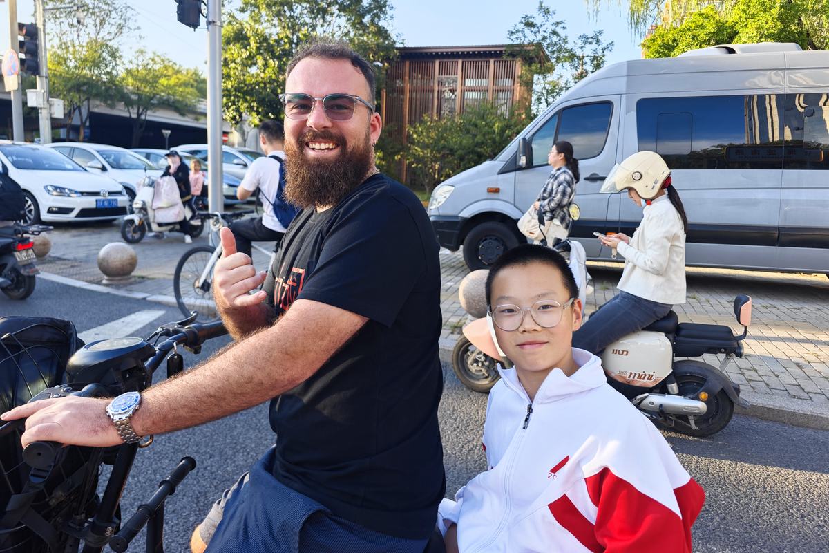 Teacher Reed giving a thumbs up on a scooter next to a smiling boy