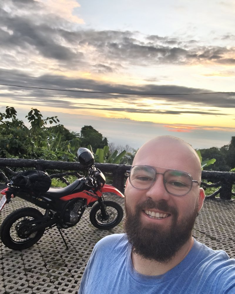 Teacher Reed smiling at a sunset viewpoint in Thailand with his motorbike
